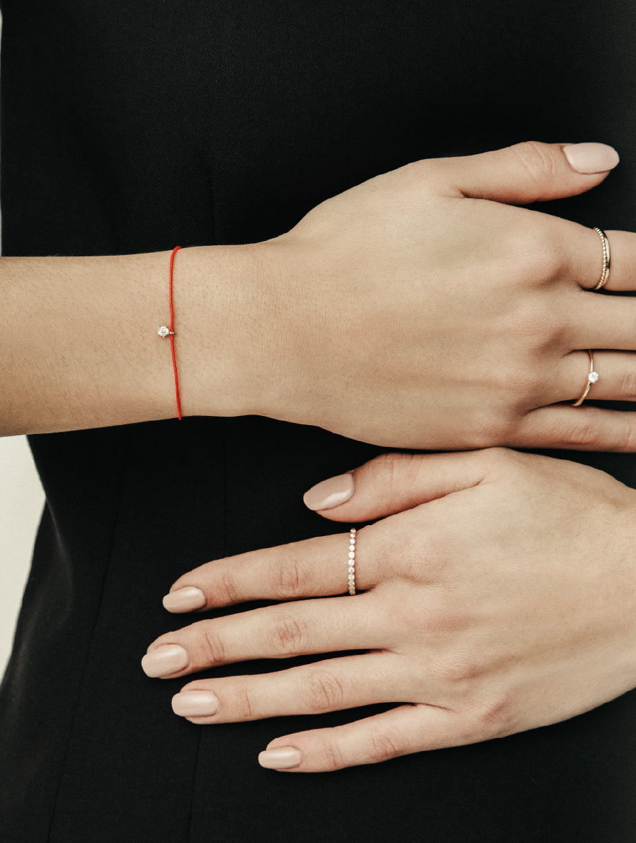 Nahaufnahme von zwei Händen eines Models mit zartem roten Armband und eleganten Ringen, aufgenommen im Studio.