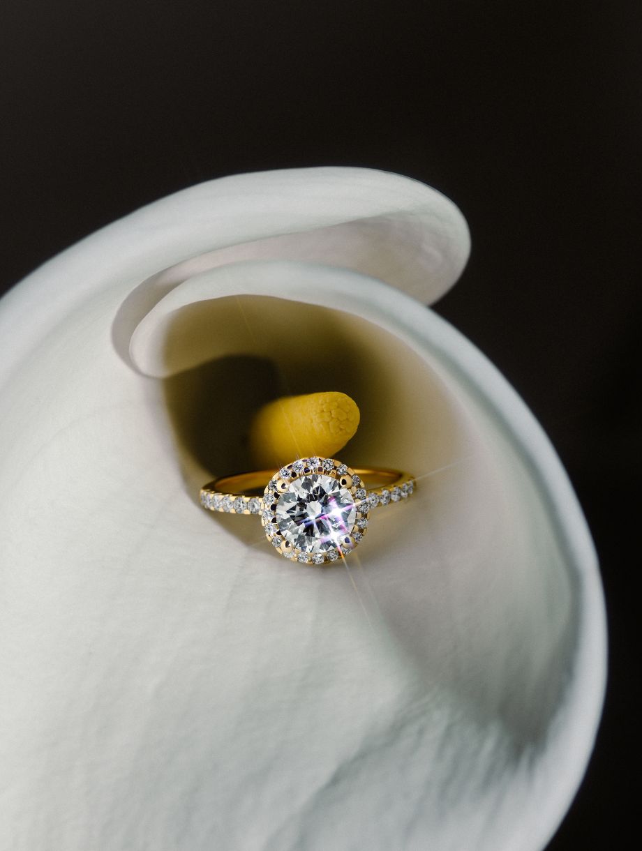 ROSE Ring DS2066G mit Diamant liegt elegant eingebettet in einer weißen Calla-Lilie.