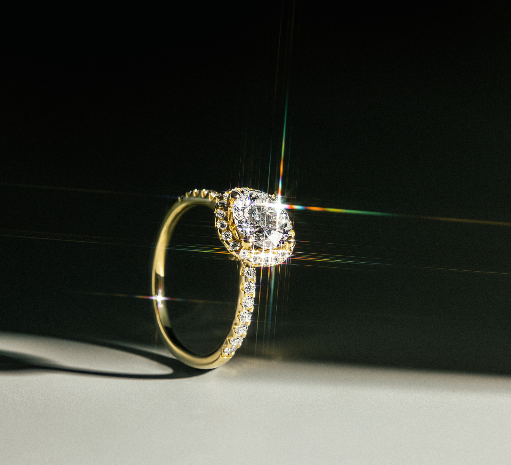 Funkelnder ROSE Ring DS2066G aus Gelbgold mit rundem Mittelstein und umlaufenden Diamanten, inszeniert auf hellem Untergrund mit dunklem Hintergrund.