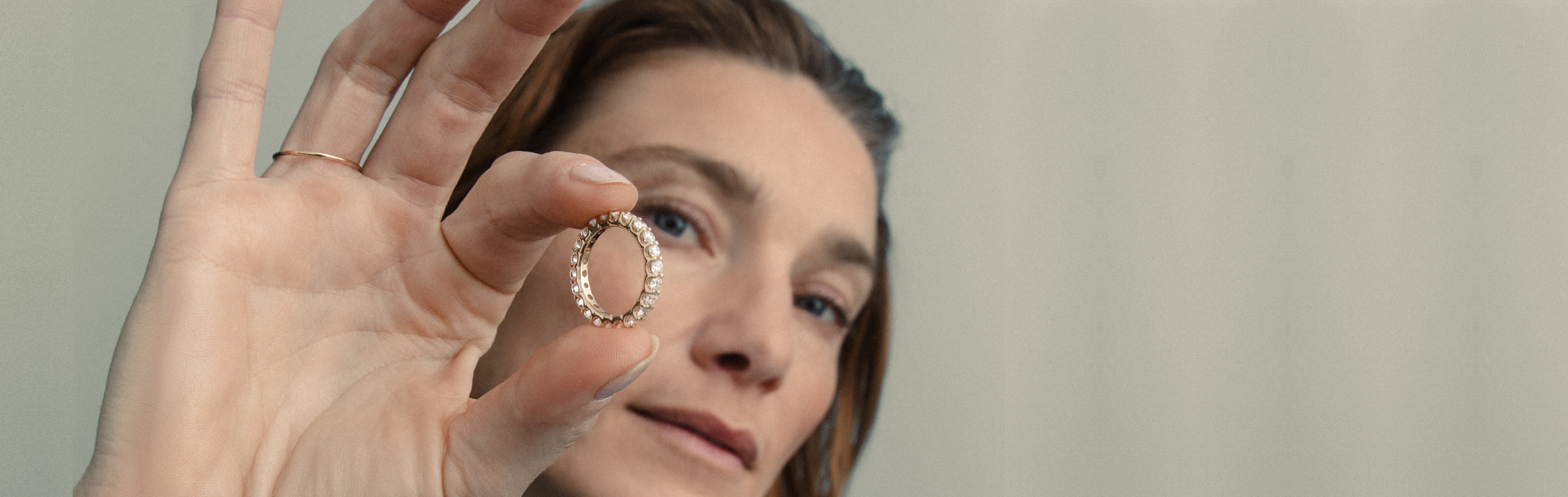 Model hält einen funkelnden Diamantring in der Hand und präsentiert ihn vor neutralem Studiohintergrund.