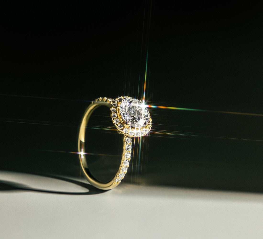 Funkelnder ROSE Ring DS2066G aus Gelbgold mit rundem Mittelstein und umlaufenden Diamanten, inszeniert auf hellem Untergrund mit dunklem Hintergrund.